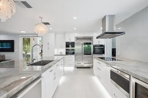 a large kitchen with granite countertop a large kitchen island a sink stainless steel appliances and cabinets