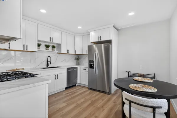 a kitchen with stainless steel appliances granite countertop a stove a sink dishwasher a refrigerator and white cabinets with wooden floor