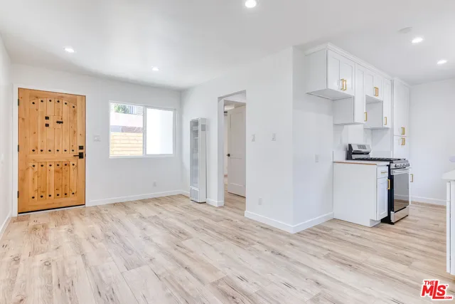 a view of empty room with wooden floor and kitchen