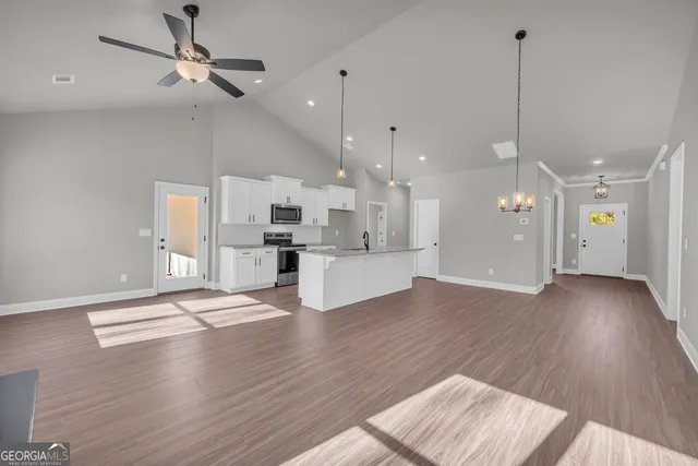 a open kitchen with kitchen island a stove a sink dishwasher a refrigerator and white cabinets with wooden floor