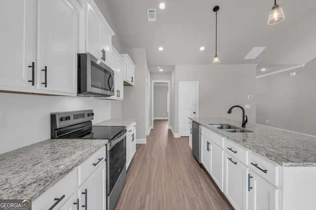 a kitchen with stainless steel appliances granite countertop wooden floors sink and white cabinets
