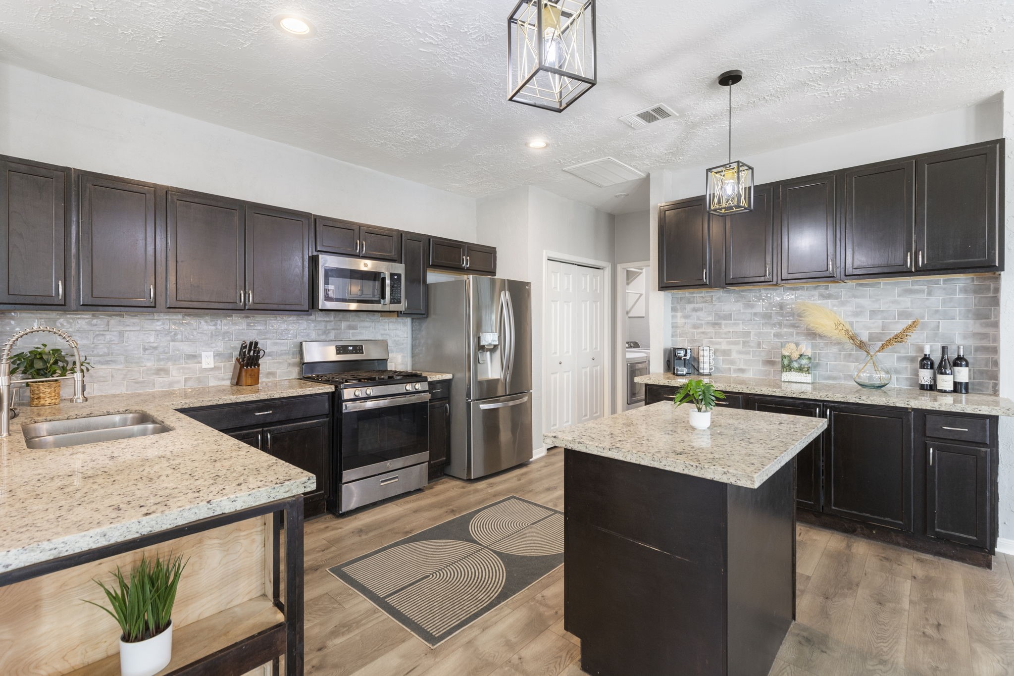 2110 Paso Rello Drive Houston, TX 77077 - Photo 16 of 41 This modern kitchen features dark wood cabinetry, stainless steel appliances, and granite countertops. It includes a central island and stylish pendant lighting, creating a functional and inviting space.