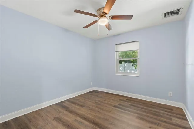 an empty room with wooden floor ceiling fan and windows