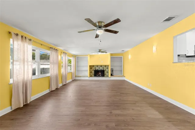 a view of a big room with wooden floor a ceiling fan and windows