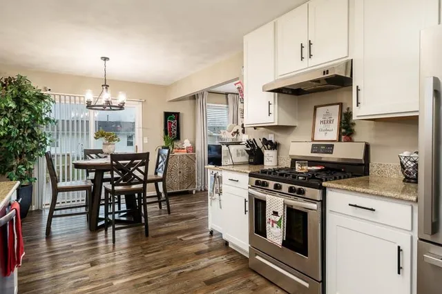 a kitchen with granite countertop a stove a sink dishwasher and white cabinets with wooden floor