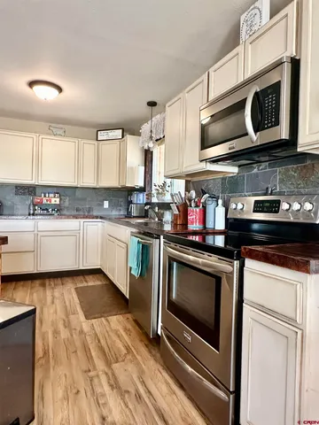 a kitchen with stainless steel appliances granite countertop a stove top oven a sink dishwasher and white cabinets with wooden floor