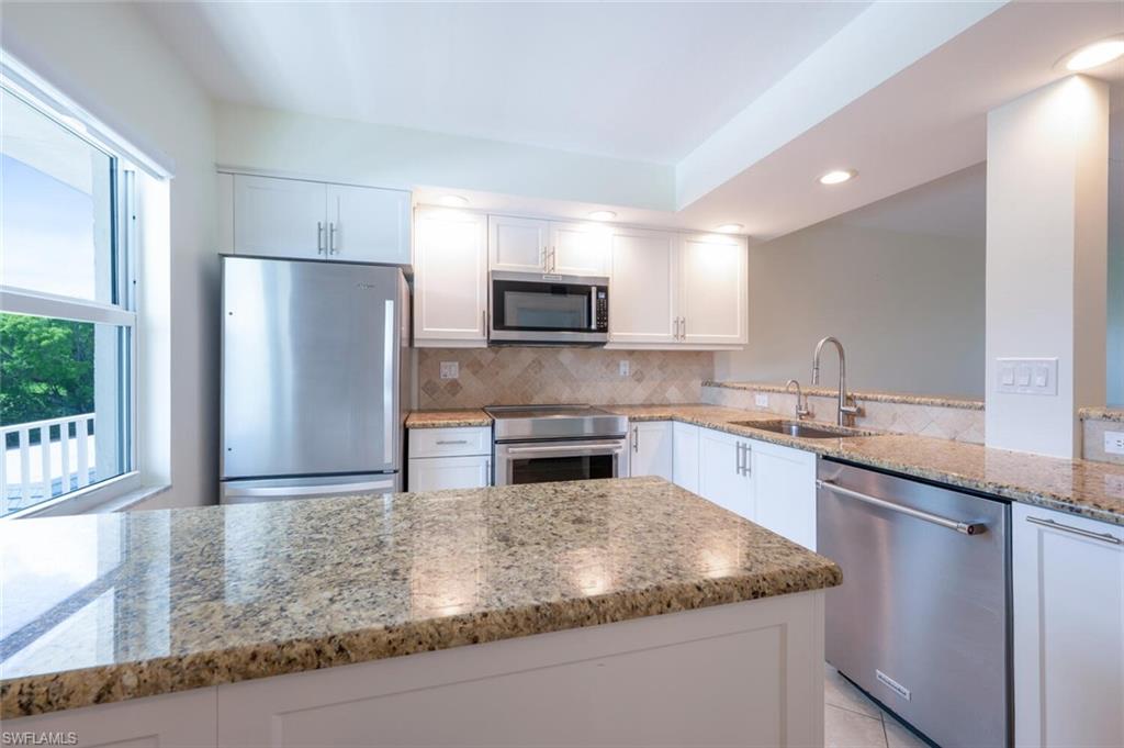 3055 Riviera Drive, Unit 306 Naples, FL 34103 - Photo 5 of 22 Kitchen featuring appliances with stainless steel finishes, white cabinets, light stone countertops, decorative backsplash, and recessed lighting