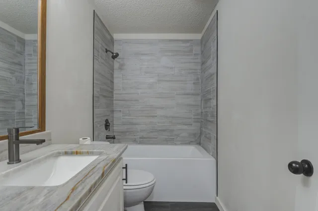 a bathroom with a granite countertop bathtub shower sink vanity and toilet