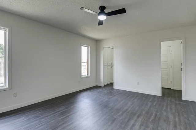 an empty room with wooden floor ceiling fan and windows
