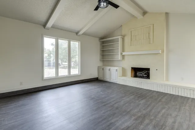 an empty room with wooden floor fireplace and windows