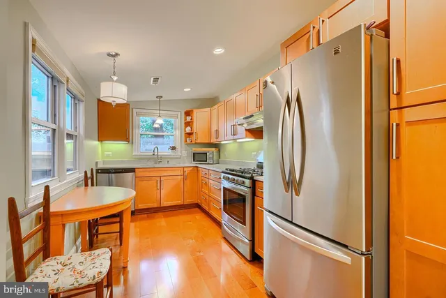 a large kitchen with stainless steel appliances granite countertop a refrigerator a oven a sink and a dining table with wooden floor