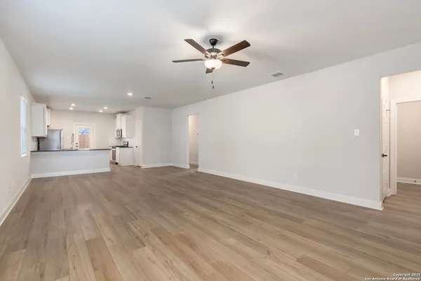 a view of an empty room with wooden floor and a ceiling fan