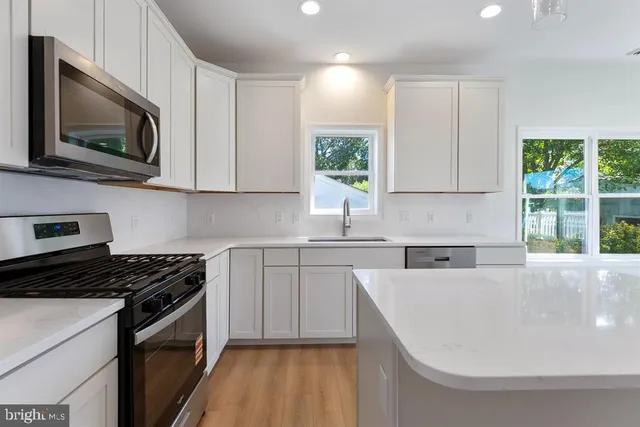 a kitchen with stainless steel appliances granite countertop a sink a stove a microwave a window and white cabinets