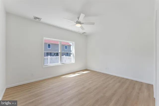 an empty room with wooden floor ceiling fan and windows