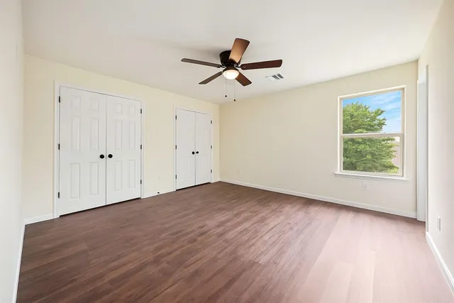 an empty room with wooden floor ceiling fan and windows