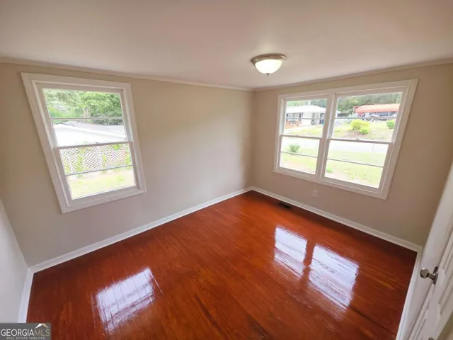 a view of an empty room with wooden floor and a window
