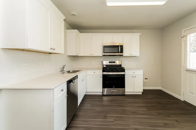 a kitchen with stainless steel appliances a stove top oven a sink a refrigerator white cabinets and wooden floor