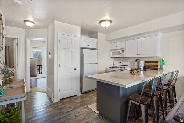 3598 North Huntsman Path, Unit 502 Eden, UT 84310 - Photo 4 of 43 Kitchen featuring a peninsula, white appliances, dark wood finished floors, white cabinetry, and a breakfast bar