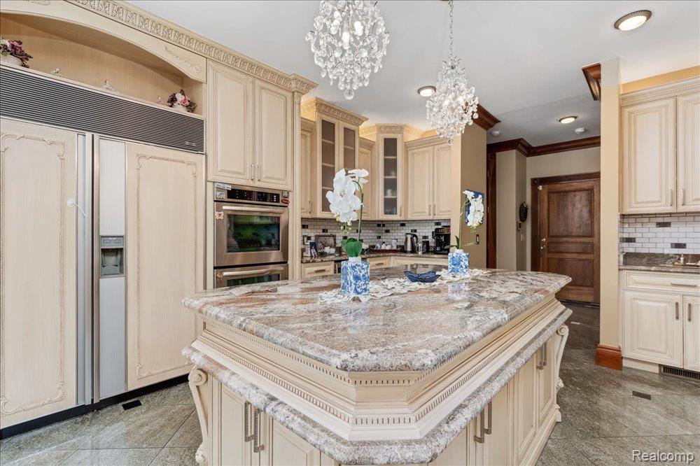 3543 Cedar Brook Drive Rochester, MI 48309 - Photo 17 of 99 Gourmet kitchen featuring a large central island with a stone countertop, built-in stainless steel appliances, custom cabinetry, and crystal chandeliers