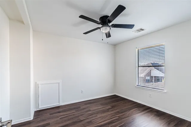 an empty room with wooden floor ceiling fan and windows