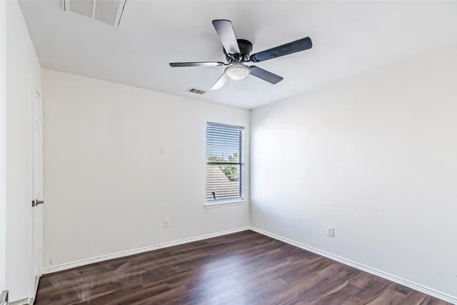 an empty room with wooden floor ceiling fan and windows
