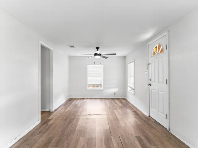 an empty room with wooden floor ceiling fan and windows
