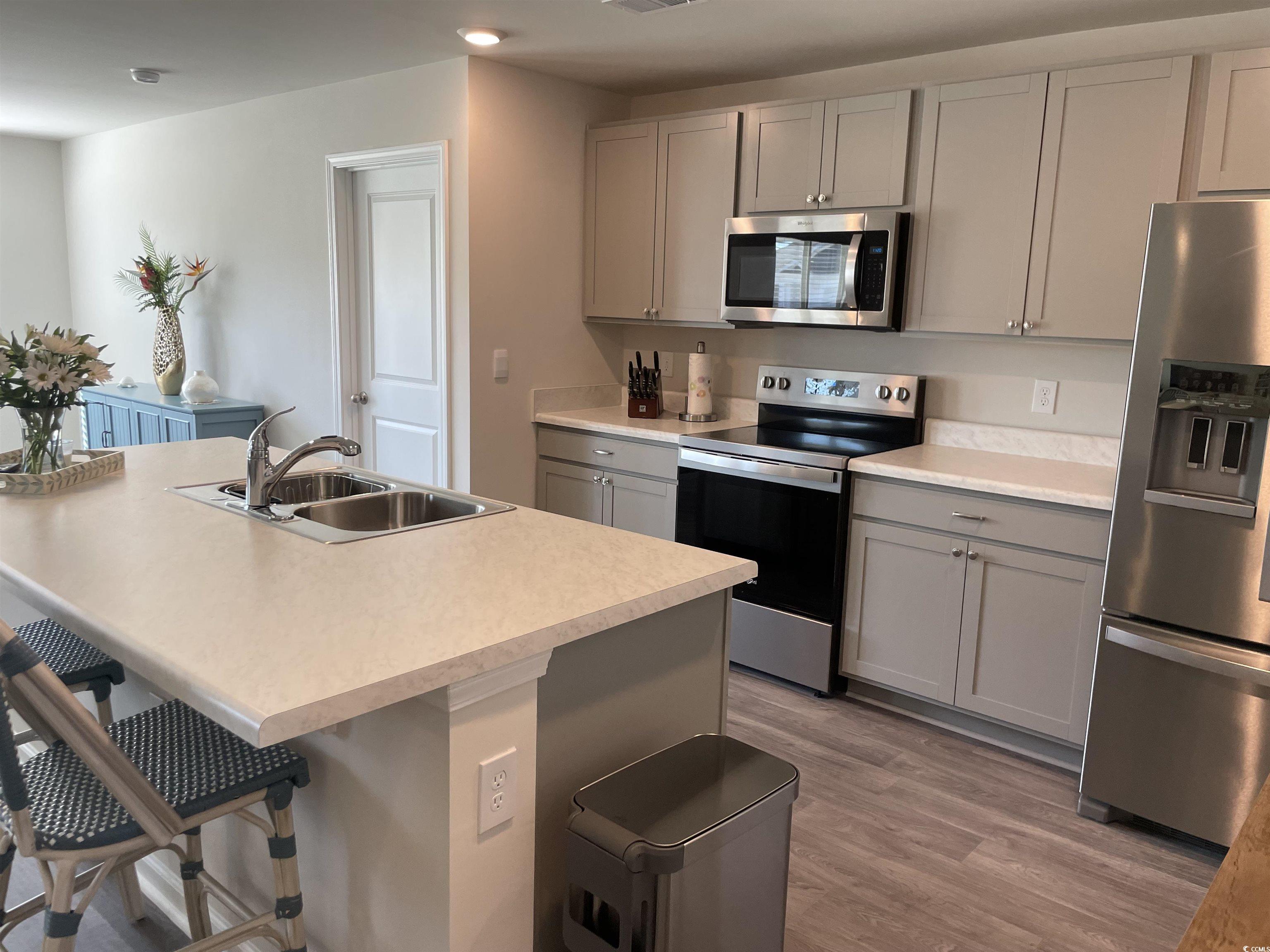 351 Jeff Waters Circle Longs, SC 29568 - Photo 7 of 33 Kitchen with gray cabinetry, appliances with stainless steel finishes, light countertops, a kitchen bar, and light wood-style flooring