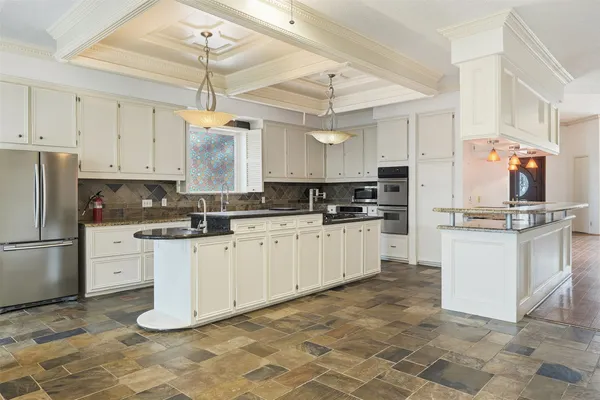 a kitchen with kitchen island granite countertop a refrigerator a stove a sink and white cabinets