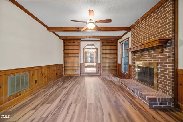 a view of an empty room with wooden floor fireplace and a window