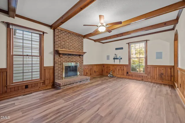 an empty room with wooden floor fireplace and windows