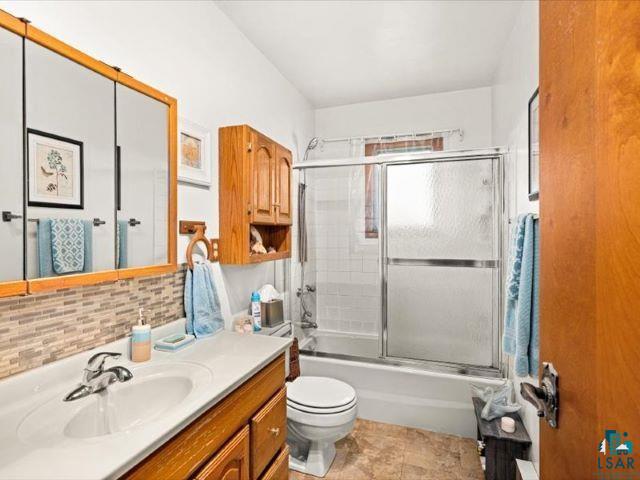 3616 Lavaque Road Hermantown, MN 55811 - Photo 28 of 43 Full bathroom featuring a single vanity with integrated sink, mosaic tile backsplash, medicine cabinet, and a shower-over-tub with sliding glass doors