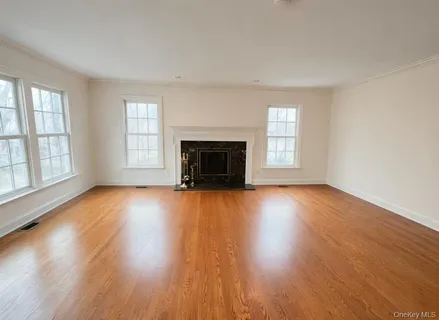 an empty room with wooden floor fireplace and windows