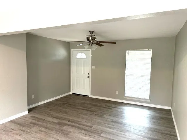 an empty room with wooden floor fan and windows