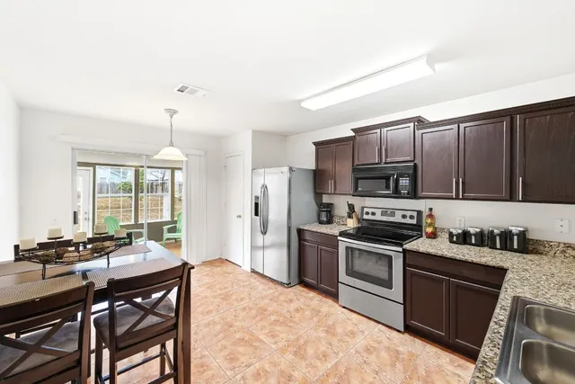 a kitchen with stainless steel appliances granite countertop a stove top oven a sink dishwasher a dining table and chairs with wooden floor