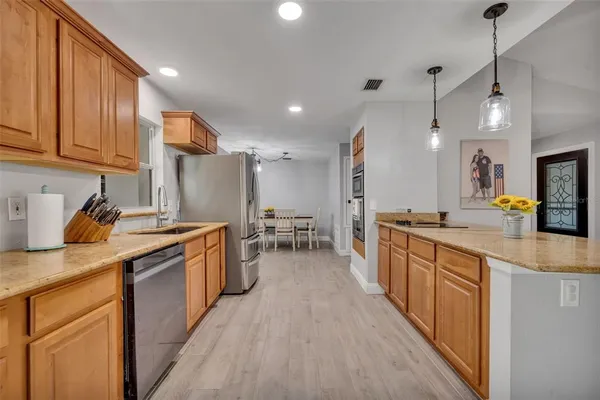 a kitchen with stainless steel appliances granite countertop wooden cabinets a sink a stove a refrigerator and island