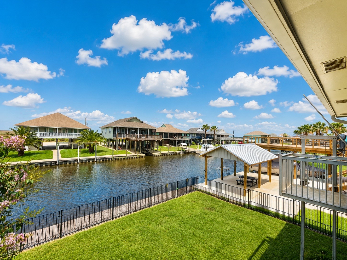 135 Sand Shoals Road Freeport, TX 77541 - Photo 4 of 20 This photo showcases a waterfront property with a canal view, featuring a neatly maintained lawn and a covered outdoor seating area. The area is lined with charming homes, and the setting offers a serene, picturesque atmosphere with clear blue skies and lush greenery.