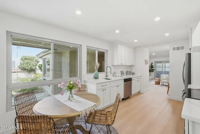 a kitchen with stainless steel appliances kitchen island granite countertop a refrigerator a stove a dining table and chairs with wooden floor