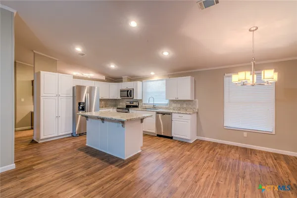 a kitchen with stainless steel appliances granite countertop a refrigerator a sink dishwasher a stove and white countertops with wooden floor