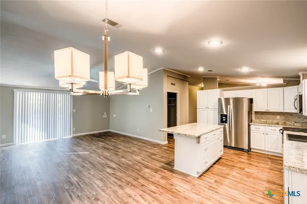 a kitchen with stainless steel appliances kitchen island granite countertop a refrigerator a sink and wooden floors