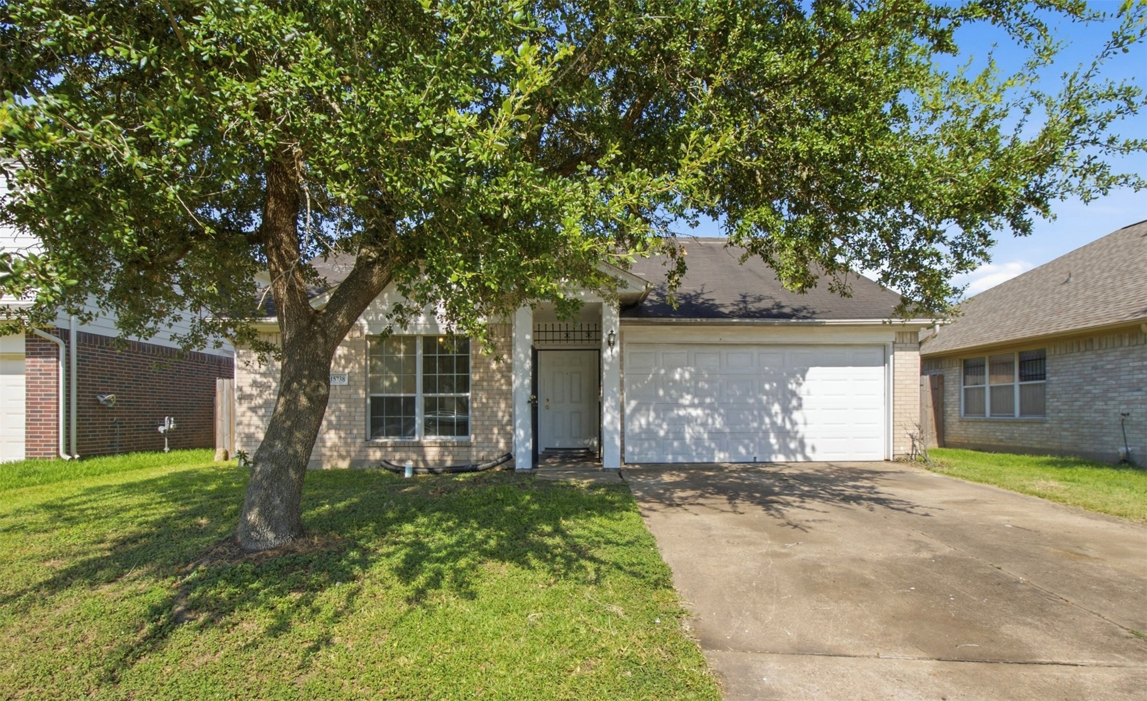Charming single-story home with a welcoming front yard shaded by a mature tree, featuring a two-car garage and a classic brick exterior.