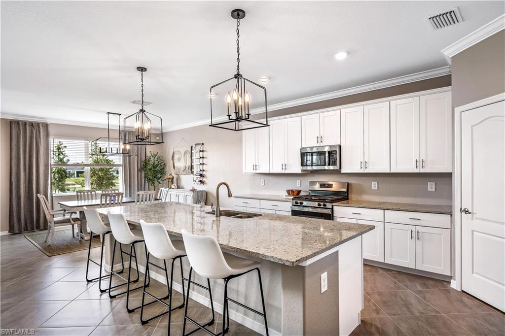 43693 Tree Top Trail Babcock Ranch, FL 33982 - Photo 11 of 25 a kitchen with stainless steel appliances granite countertop a sink a stove a kitchen island with chairs and cabinets