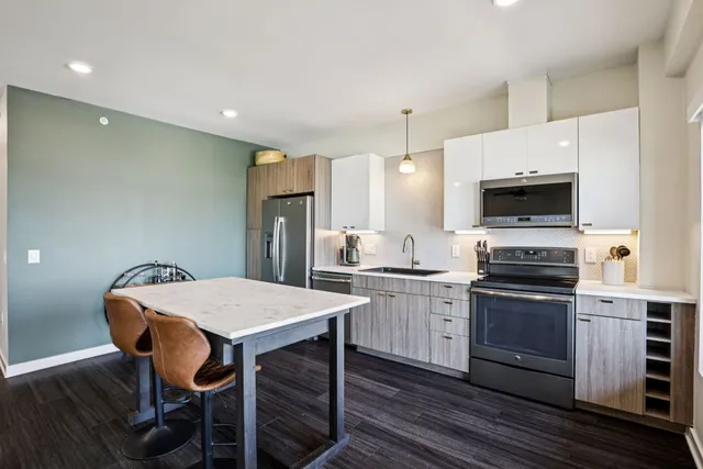 a kitchen with stainless steel appliances granite countertop a refrigerator a sink a stove a dining table and chairs