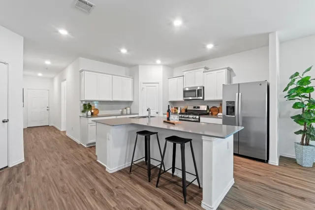 a kitchen with stainless steel appliances granite countertop a refrigerator a stove top oven a sink dishwasher and white cabinets with wooden floor