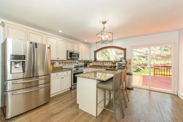a kitchen with stainless steel appliances granite countertop a refrigerator a stove a sink and white cabinets with wooden floors