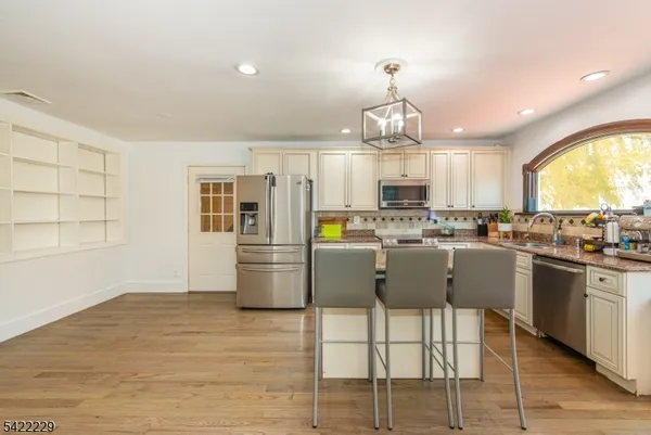 a kitchen with stainless steel appliances kitchen island granite countertop a refrigerator a stove top oven a sink dishwasher and white cabinets with wooden floor