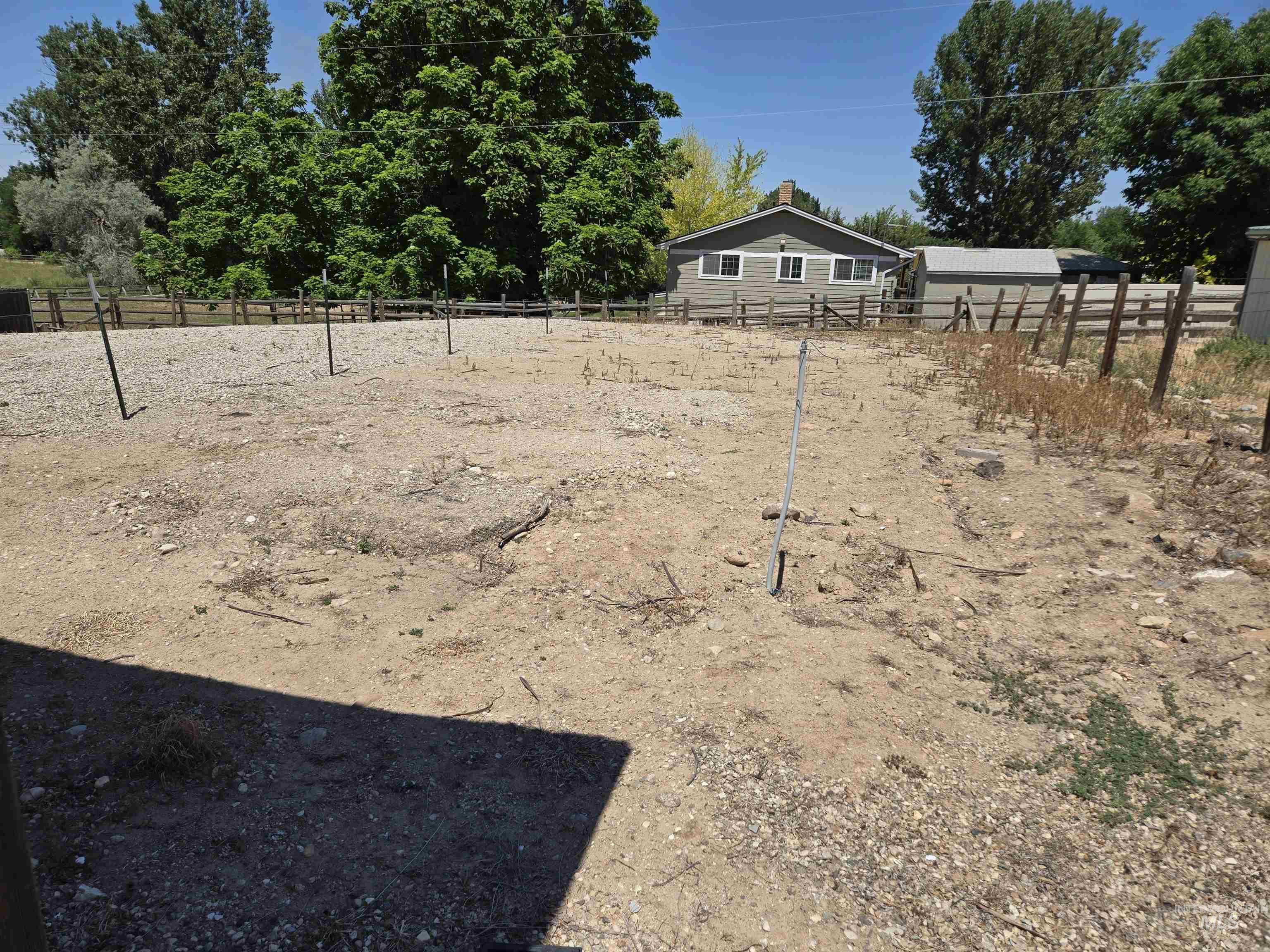 12050 West Hidden Valley Rim Road Boise, ID 83709 - Photo 31 of 39 Expansive gravel lot with a sturdy wood fence, bordered by mature trees