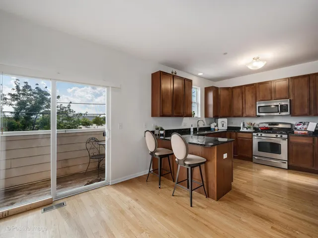 a kitchen with stainless steel appliances granite countertop a stove top oven a sink dishwasher a dining table and chairs with wooden floor