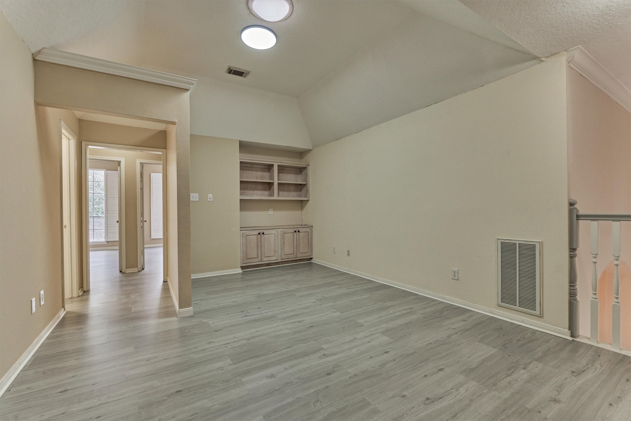 14420 Walters Road, Unit 26 Houston, TX 77014 - Photo 23 of 45 This photo showcases the upstairs game room or office space with high ceilings, a skylight, and wood-look flooring. It features built-in shelving, providing ample storage space. An adjacent hallway leads to additional bedrooms, and large windows allow natural light to fill the space.