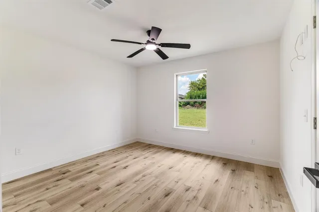 an empty room with wooden floor ceiling fan and window