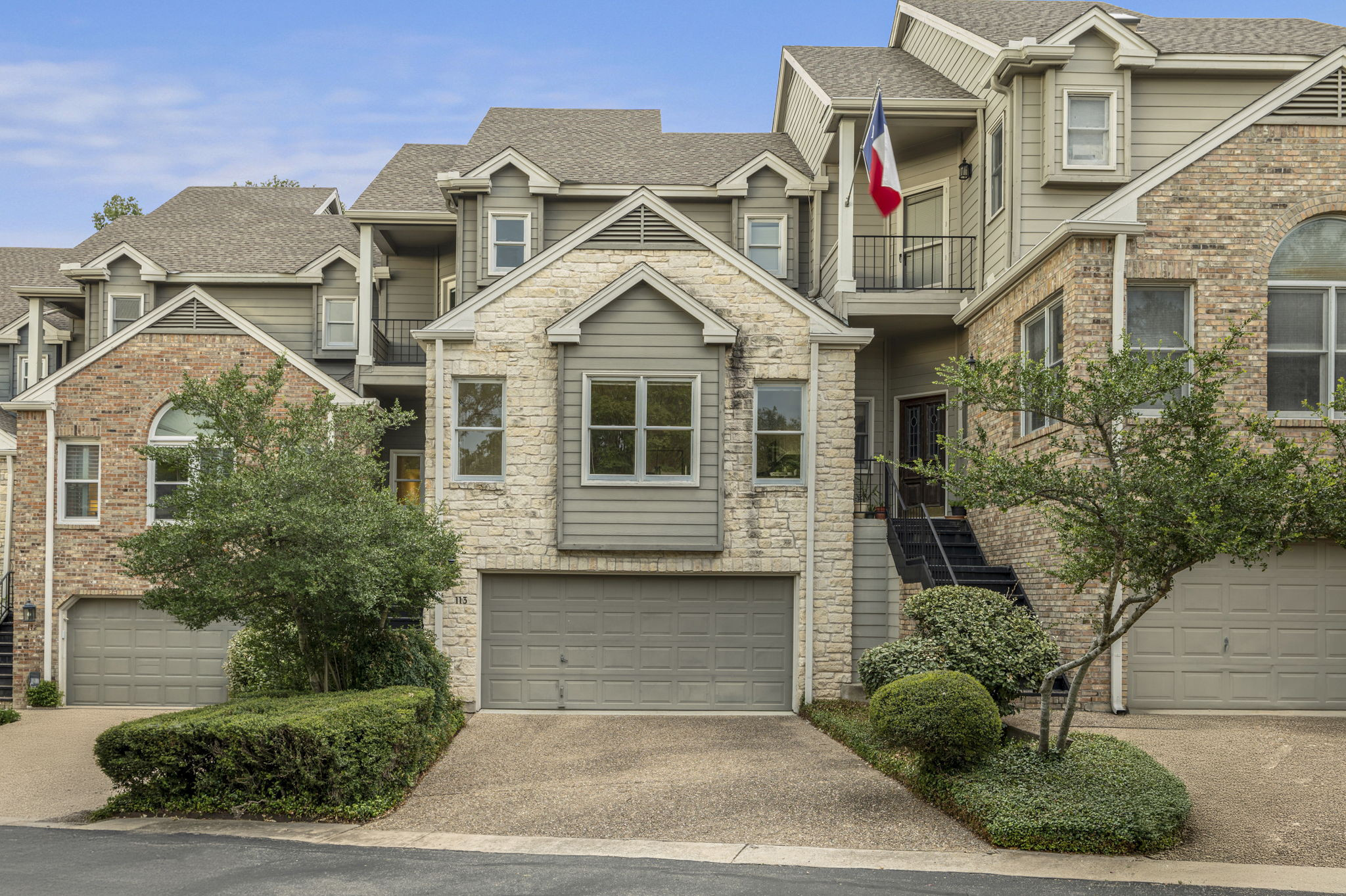 6010 Long Champ Court, Unit 113 Austin, TX 78746 - Photo 10 of 25 Craftsman house with a balcony, driveway, roof with shingles, an attached garage, and stone siding